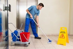 45703699 - happy male janitor with cleaning equipments mopping floor